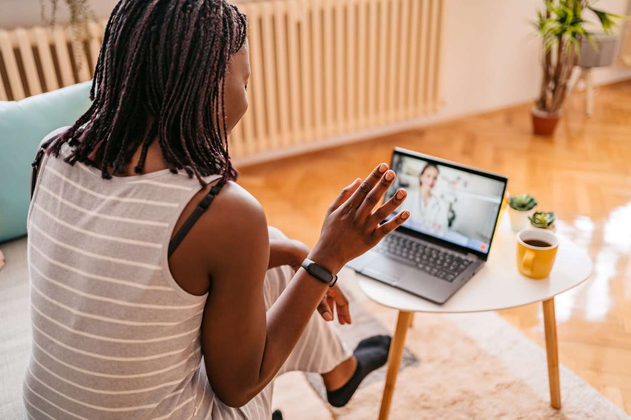 African-American woman Video Conferencing With Doctor On laptop while sitting on sofa in her home.